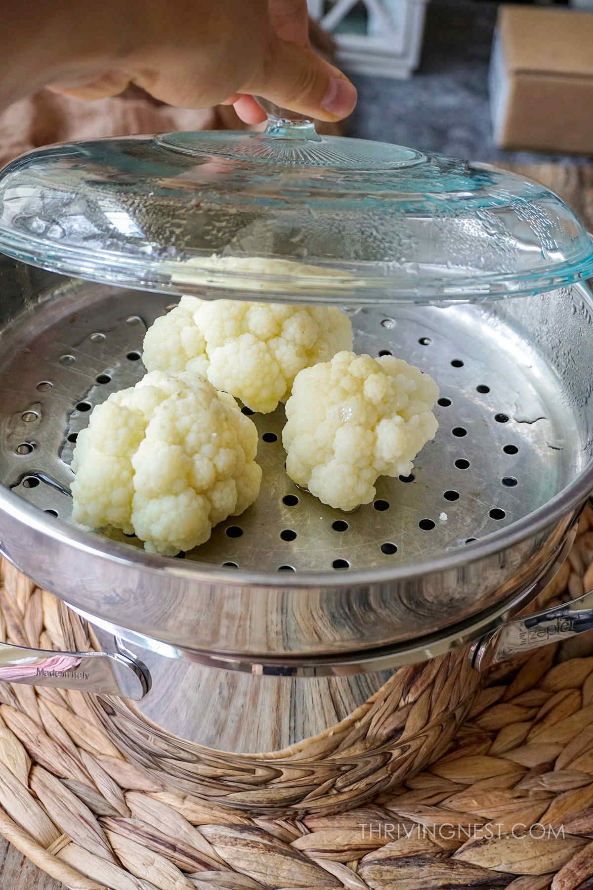 Steaming cauliflower florets in a pot with steaming basket and covered with a lid.