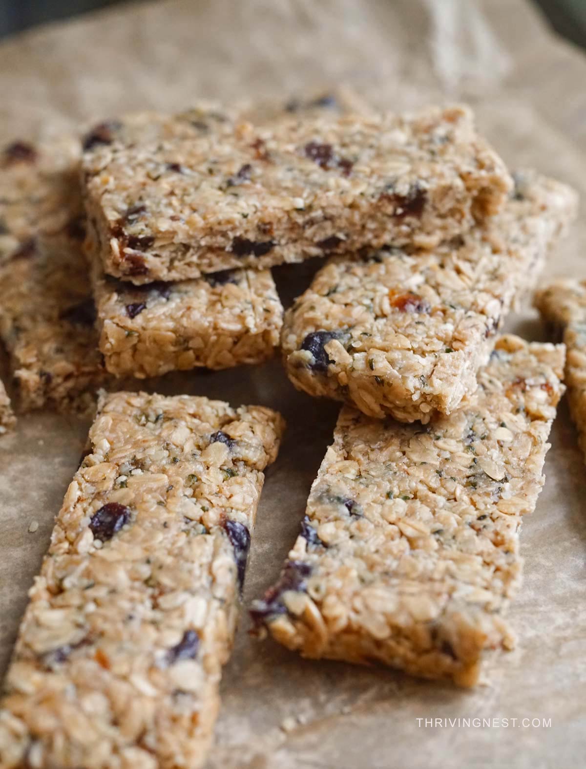 Homemade no-bake snack bars with oats, prunes, cashew butter nuts and hemp seeds stacked on a board with parchment paper-close up shot