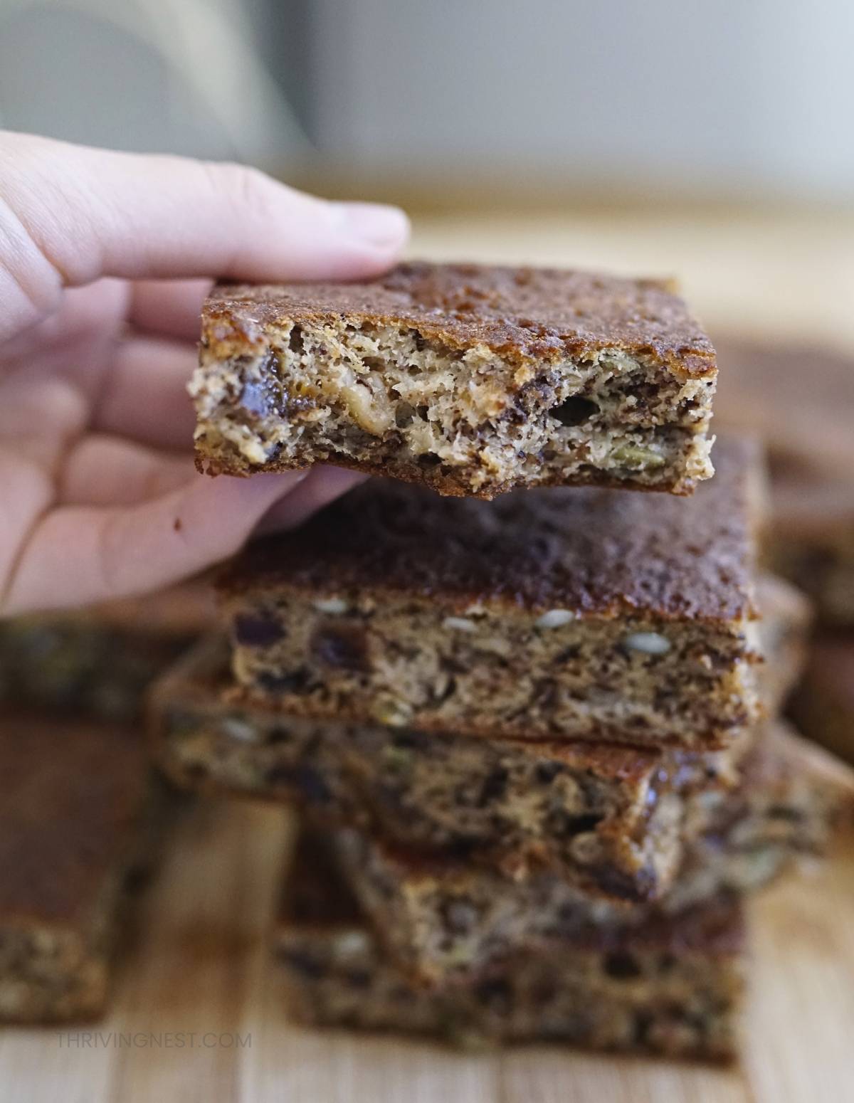 Stack of thick banana pancake squares made with ripe bananas, yogurt, walnuts, pumpkin seeds,  chopped prunes, showing the moist texturized close-up bite texture